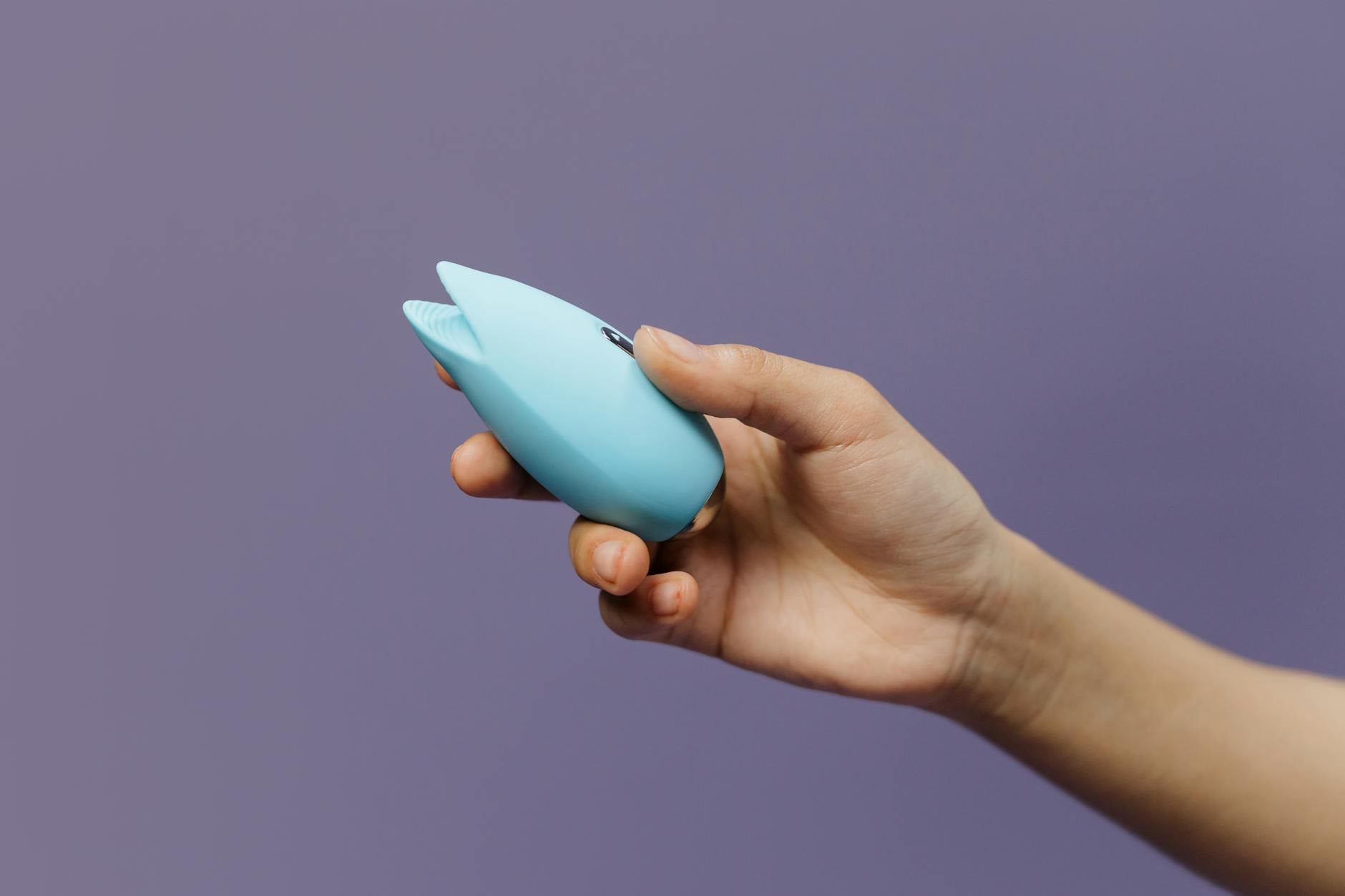 A hand holding a blue silicone vibrator against a purple background, symbolizing self-pleasure and personal satisfaction