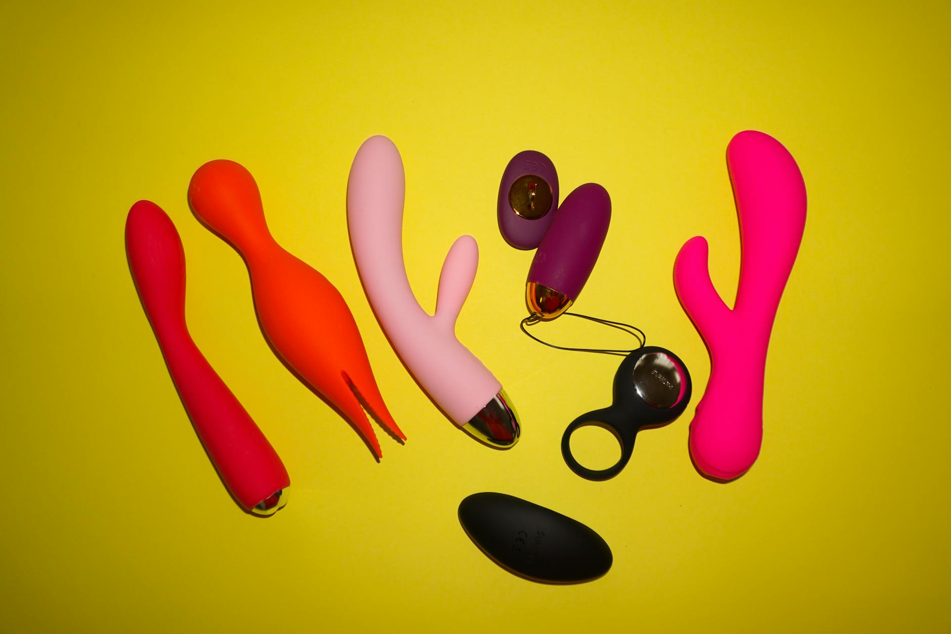 Colorful clitoral vibrators displayed on a bright yellow background, showcasing design diversity